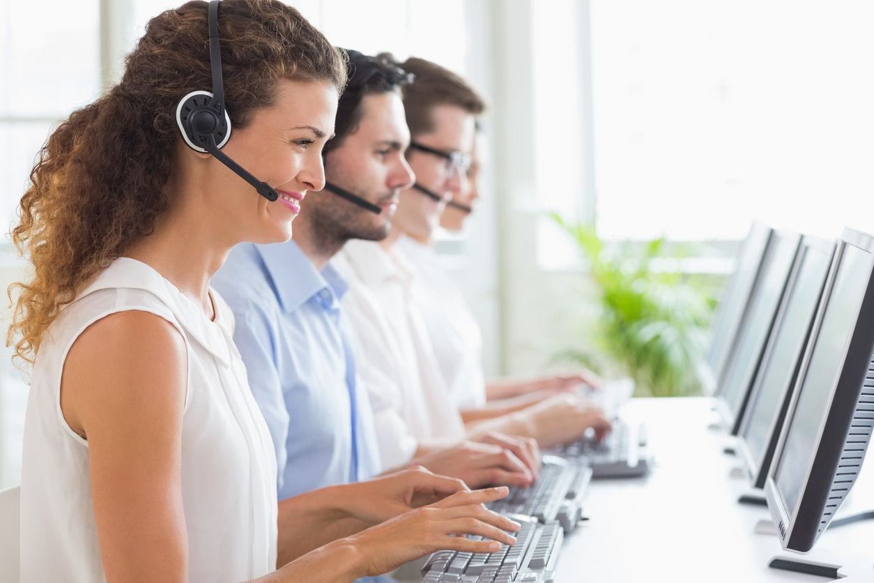 A group of people with headsets on working at computers.