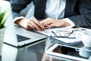 Person analyzing financial documents with laptop and glasses on desk.