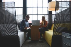 Two coworkers discussing laptop in office booth