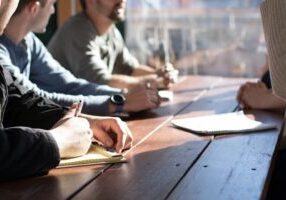 Colleagues writing notes at sunlit meeting table